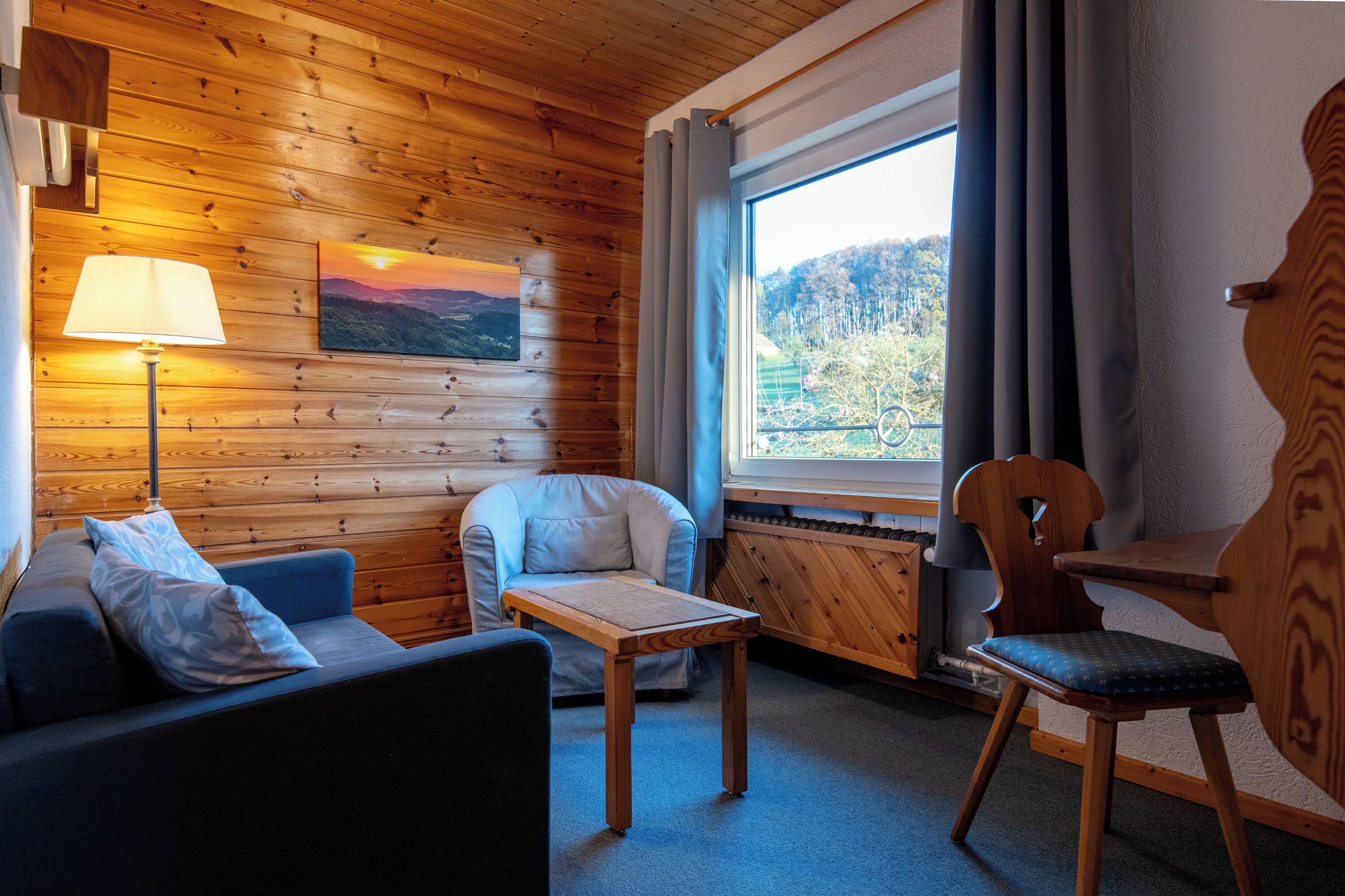 A cozy room with a wooden interior, a sofa, a chair, a table, and a window with a view of the outdoors.
