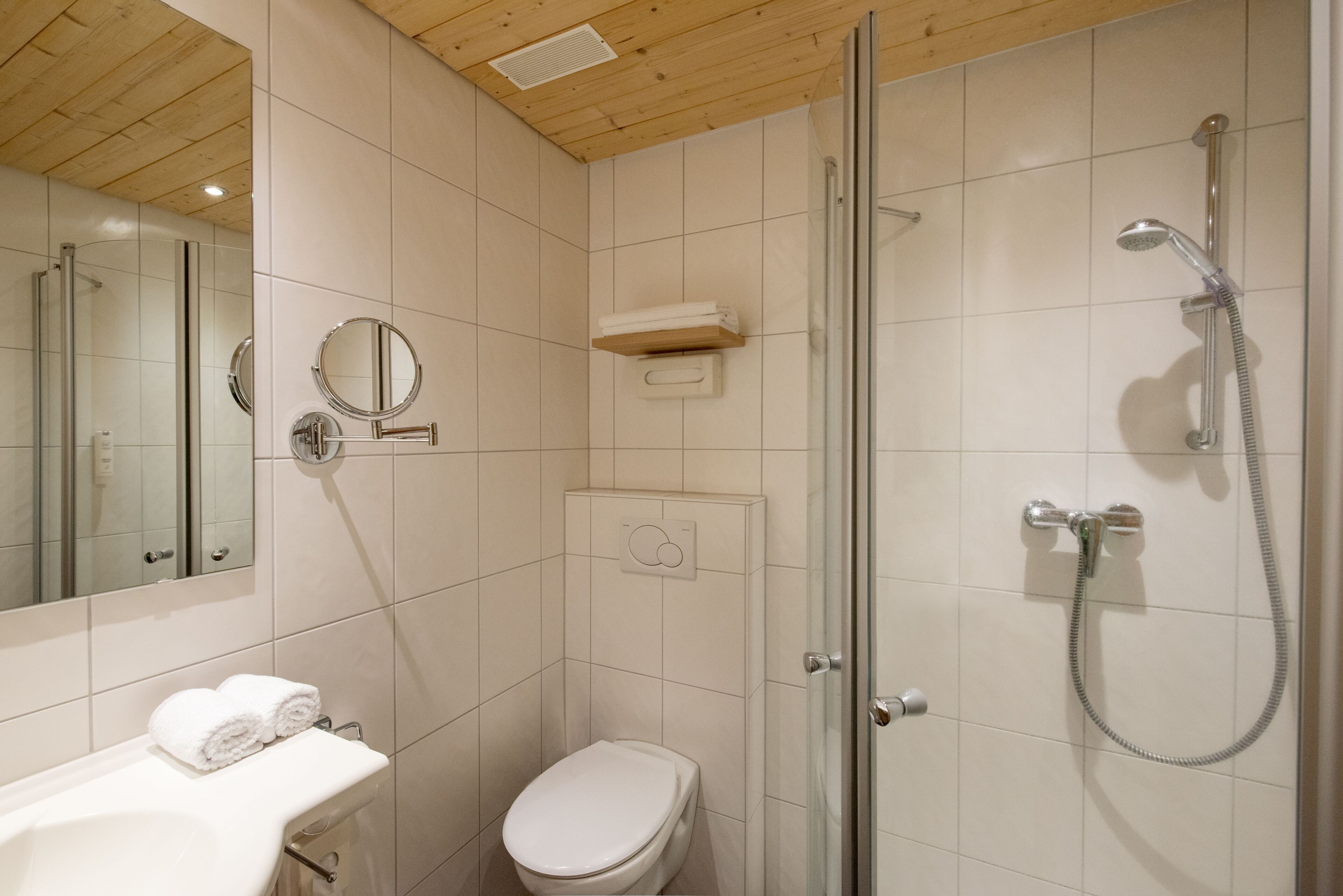 Un baño con inodoro, lavamanos con toallas, espejo, ducha con puerta de cristal y toallero.