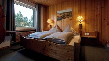 Una habitación con paneles de madera, una cama, dos lámparas de noche, una ventana y un cuadro en la pared.
