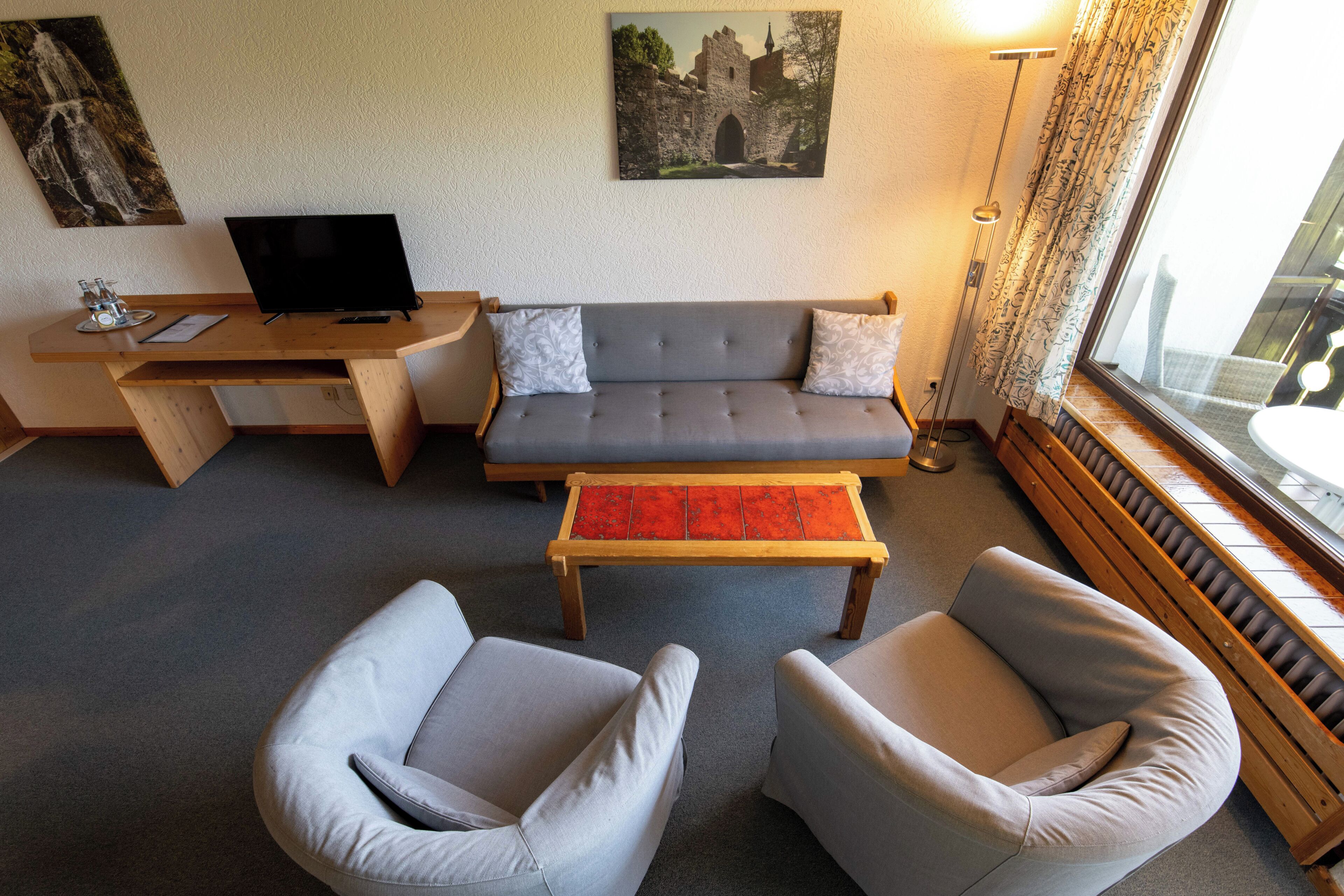 A living room with a sofa, two armchairs, a coffee table, a TV, and artwork on the walls.