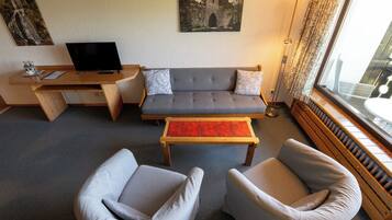 A living room with a sofa, two armchairs, a coffee table, a TV, and artwork on the walls.