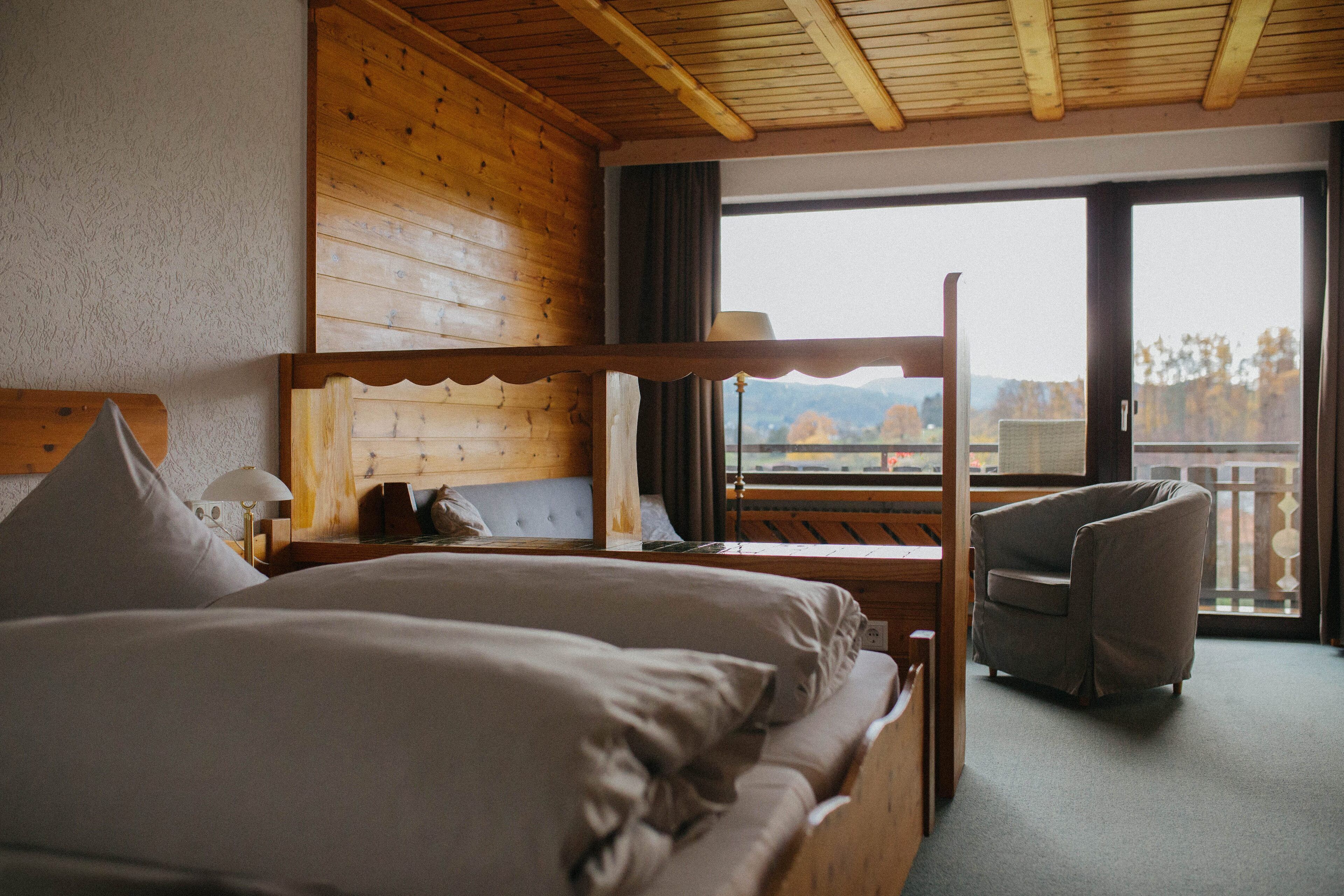 Habitación de hotel con una cama nido de madera, una silla, una ventana con vistas a montañas y un balcón.