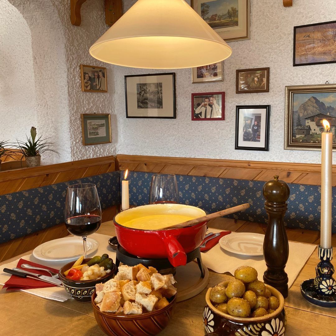 A dining table with a red pot, a candle, a glass of wine, and bowls of food.