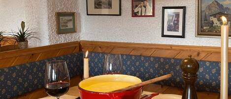 A dining table with a red pot, a candle, a glass of wine, and bowls of food.