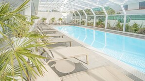 En indendørs swimmingpool med liggestole og palmeplanter.