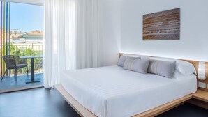 Et moderne hotelværelse med en stor seng, en balkon med en stol og udsigt til bygninger.
