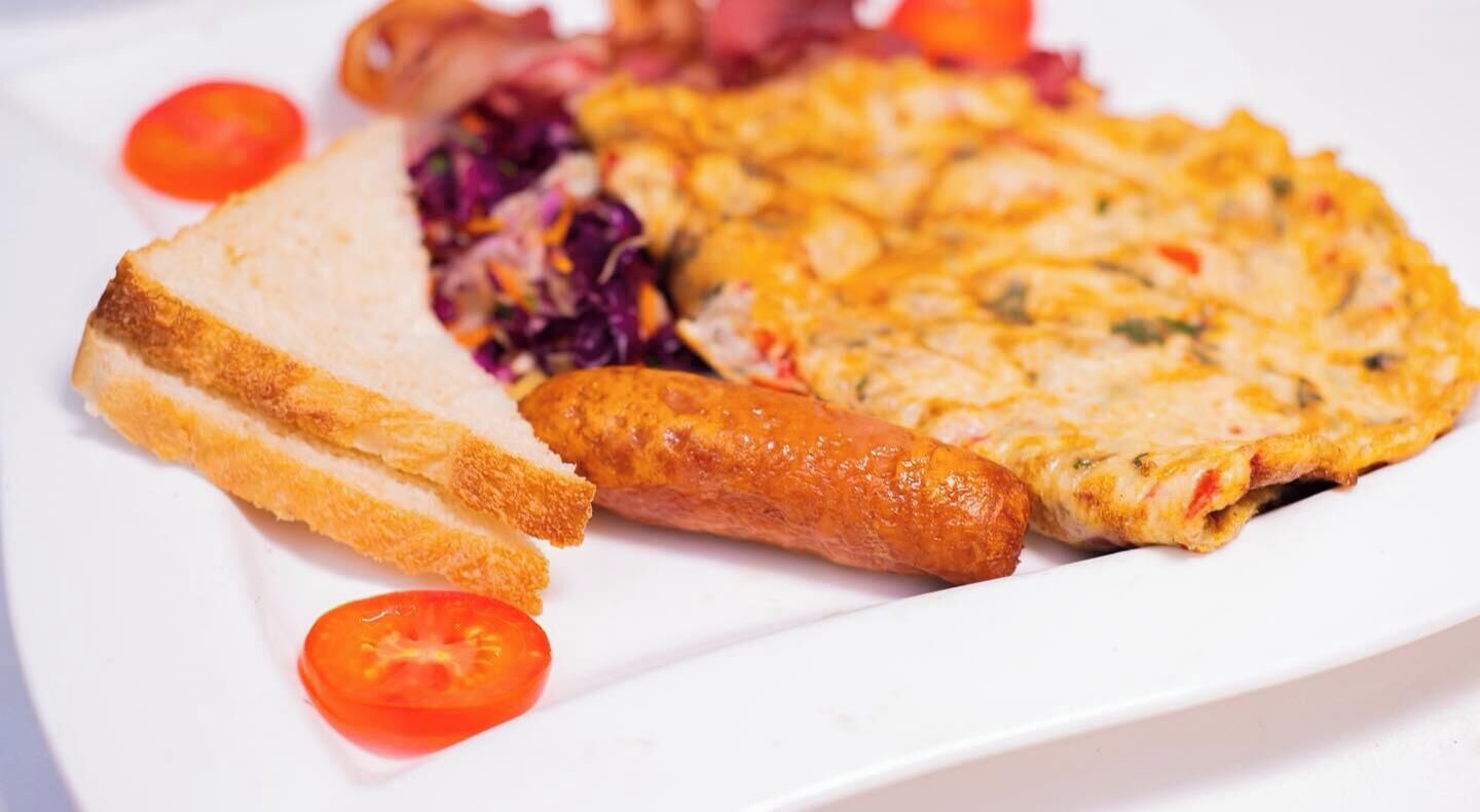 A plate with a slice of bread, a sausage, a slice of omelette, and some vegetables.