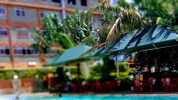 A swimming pool with metal railings, surrounded by palm trees and a building with multiple windows. - Dillons Highway Motel (Kilimambogo)