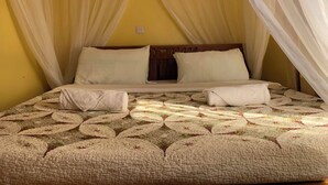 A bed with a canopy, a quilt with a floral pattern, and a wooden headboard. - Dillons Highway Motel (Kilimambogo)
