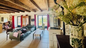 Una sala rústica con vigas de madera a la vista, un sofá, una mesa de centro y una planta grande en maceta.