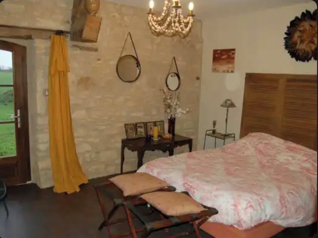 Une chambre à coucher avec un lit, un banc en bois, un lustre et un miroir au mur.