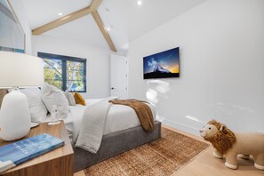 Une chambre à coucher moderne avec un lit, une télévision, une fenêtre et un jouet en peluche.