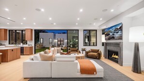 Ein großzügiger Wohnbereich mit einem weißen Sofa, einem Kamin und einem Essbereich, der durch große Fenster sichtbar ist.