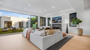 Ein modernes Wohnzimmer mit einem großen weißen Sofa, einem Kamin und Blick auf Garten und Pool.