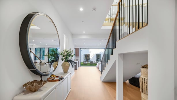 Ein modernes Interieur mit einem langen Flur, einem großen runden Spiegel und einer Treppe, die zu einer oberen Ebene führt.