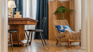 Un coin repas avec une table en bois, deux chaises noires, une lampe et un fauteuil en osier agrémenté d’un coussin bleu et blanc.