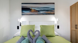 A hotel room with a bed, green bedding, a painting of a landscape, and a heart-shaped towel arrangement. - Holiday Apartment 'El Alcaidón 1' with Wi-Fi and Air Conditioning (Tías)