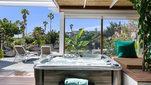 A hot tub with a wooden deck, lounge chairs, and a view of palm trees and rocks. - Holiday Apartment 'El Alcaidón 1' with Wi-Fi and Air Conditioning (Tías)