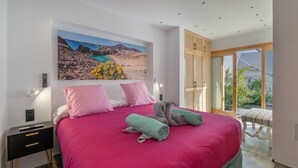 A bedroom with a large bed, a painting of a coastal landscape, a nightstand, and a view through a glass door. - Holiday Apartment 'El Alcaidón2' with Wi-Fi and Air Conditioning (Tías)