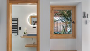 A modern bathroom with a wooden door, a towel rack, a sink, a mirror, and a window with a view of palm trees. - Holiday Apartment 'El Alcaidón2' with Wi-Fi and Air Conditioning (Tías)