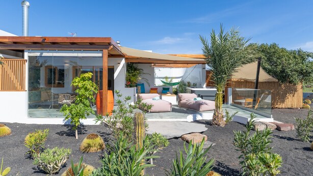 A modern house with a glass facade, a wooden deck, and a garden with various plants. - Holiday Apartment 'El Alcaidón2' with Wi-Fi and Air Conditioning (Tías)