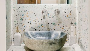 Un bagno con un lavabo di pietra grande e rotondo, uno specchio sopra e una porta in legno sullo sfondo.