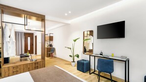 Una camera d'albergo moderna con un armadio in legno, una scrivania con una sedia, uno specchio grande, una TV a schermo piatto e una pianta in vaso.