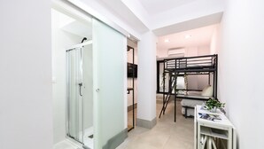A modern hotel room with a glass shower door, a bunk bed, a small table with a plant, and a white cabinet. - (RJS3) Cozy Studio in Salamanca District (Madrid)