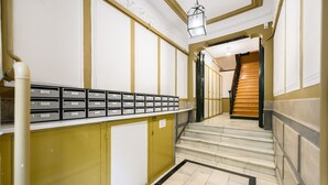 Un pasillo con una escalera que conduce a una plataforma. Hay armarios de almacenamiento a lo largo de la pared y una fila de buzones.