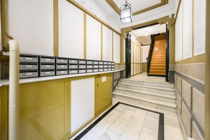 Ein Flur mit einer Treppe, die zu einer Zwischenebene führt. An der Wand befinden sich Stauraumschränke und eine Reihe von Briefkästen.