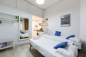 A hotel room with two beds, a washing machine, a small kitchenette, and a cityscape picture on the wall. - (PIZ401) Cozy Studio in the Center of Madrid (Madrid)