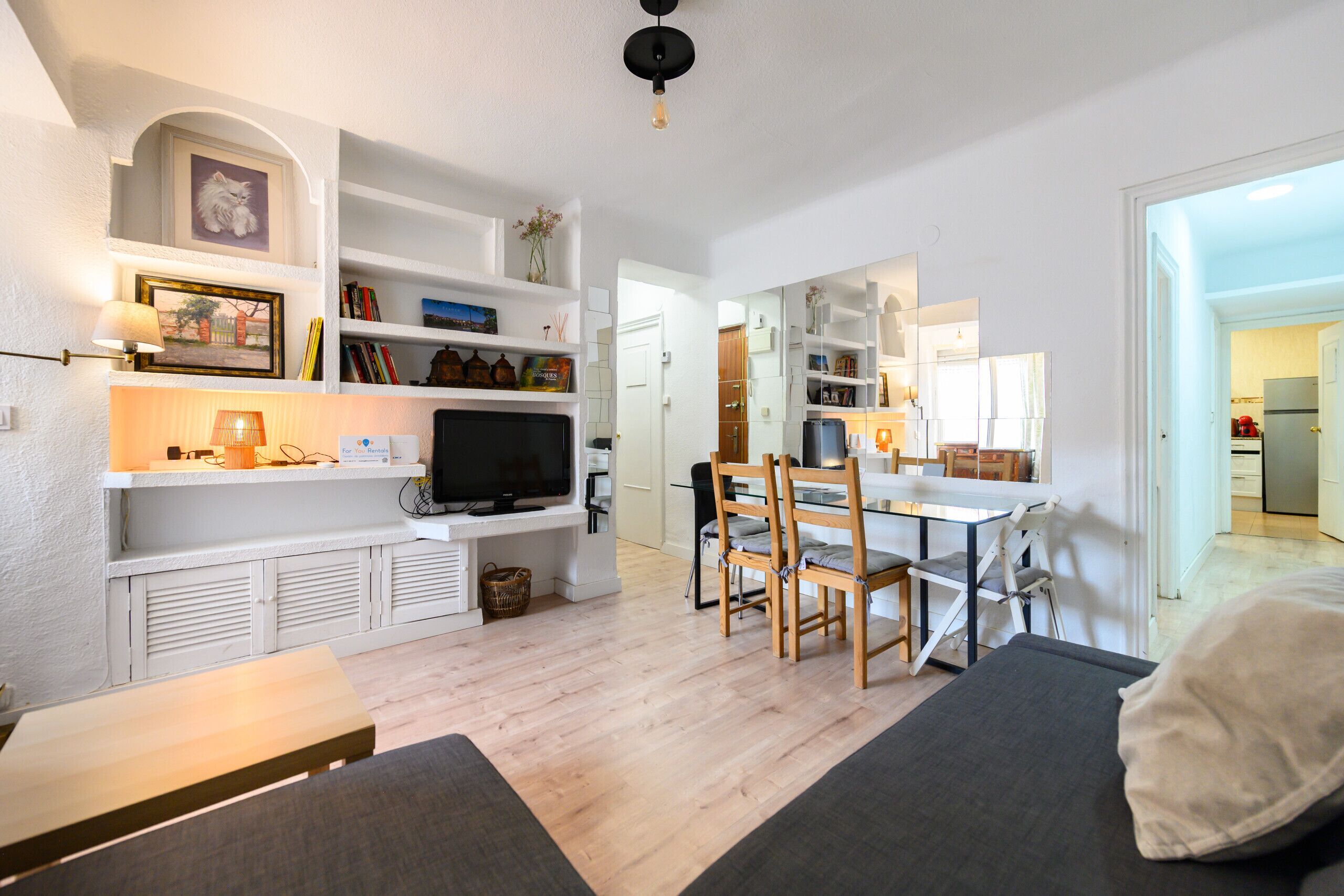 Una sala de estar moderna con una televisión de pantalla plana, sillas de madera, un sofá y una mesa de comedor.