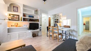 Una sala de estar moderna con una televisión de pantalla plana, sillas de madera, un sofá y una mesa de comedor.