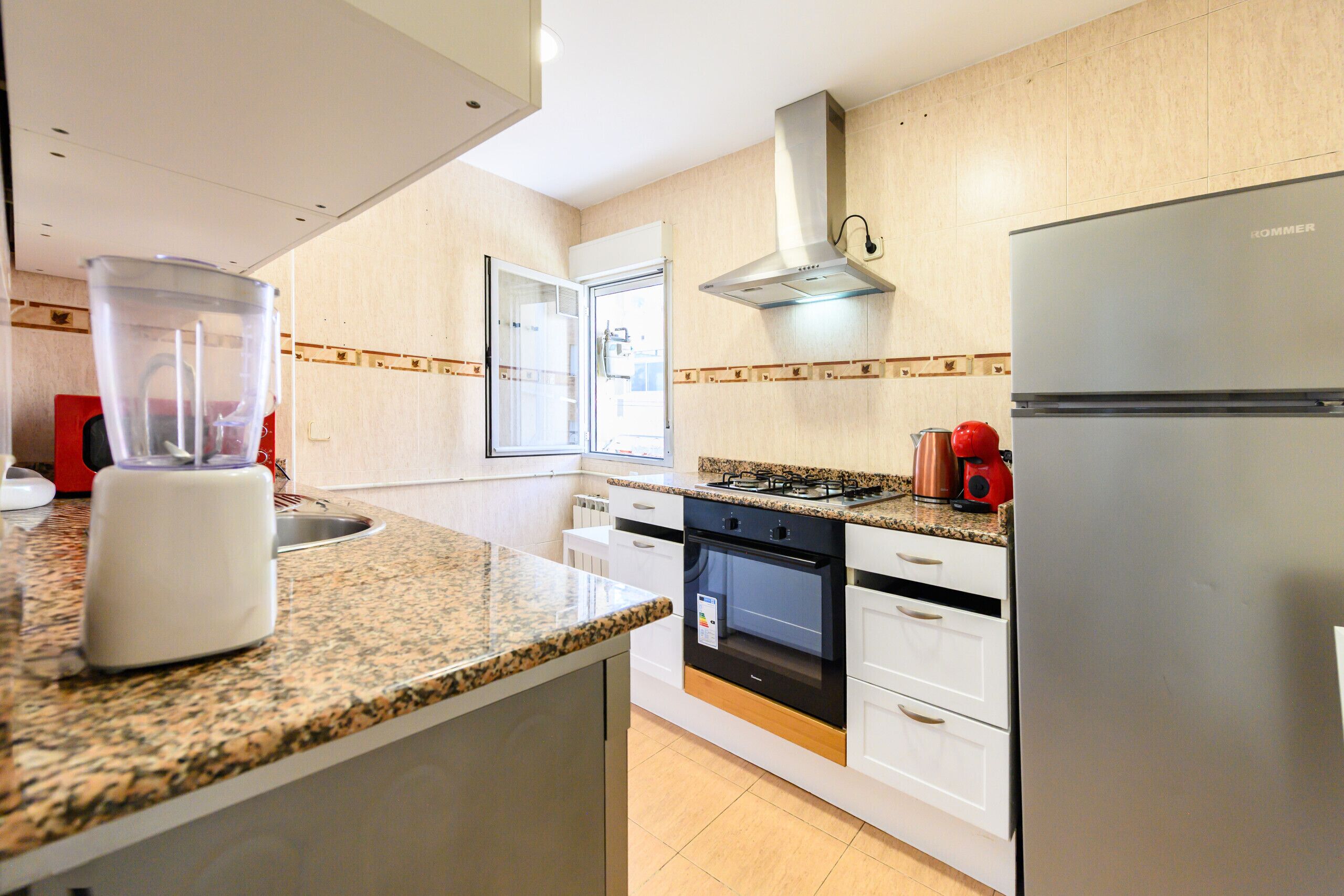 Una cocina moderna con encimeras de granito, horno empotrado, refrigerador de acero inoxidable y ventana con vistas.