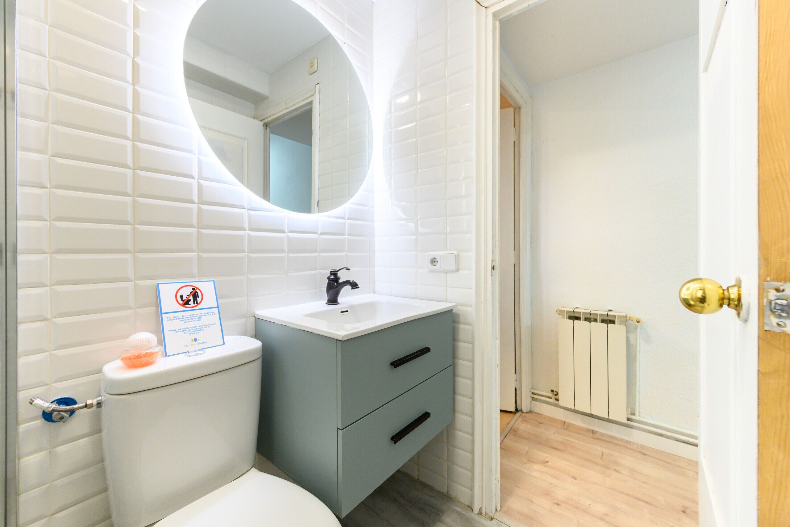 A bathroom with white tiled walls, a white toilet, a grey sink with a mirror above it, and a radiator on the wall.