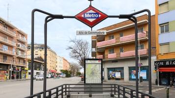 A metro station entrance with a map display, a sign for 'Alto de Extremadura', and surrounding buildings.