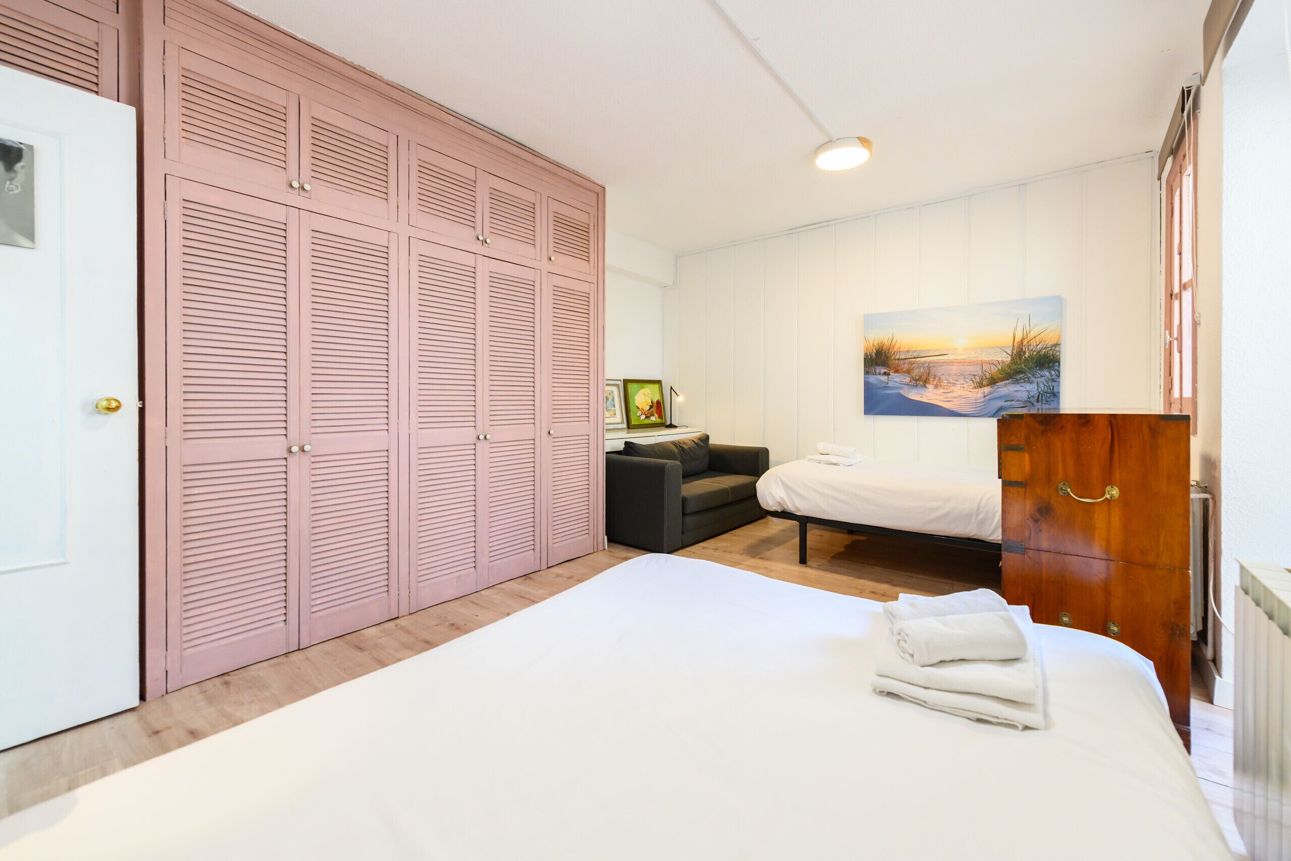 A bedroom with a large bed, a wardrobe, a sofa, and a painting on the wall.