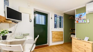 A compact room with a dining table set for two, a TV mounted on the wall, a green door, and a wooden dresser. - (SVF1304) Cozy Studio in the Center of Madrid (Madrid)
