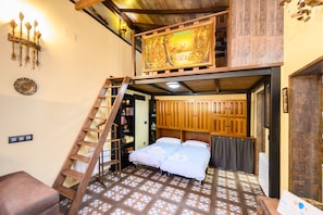 Un dormitorio con cama tipo altillo, escalera de madera, un cuadro sobre la cama y suelo de baldosas.