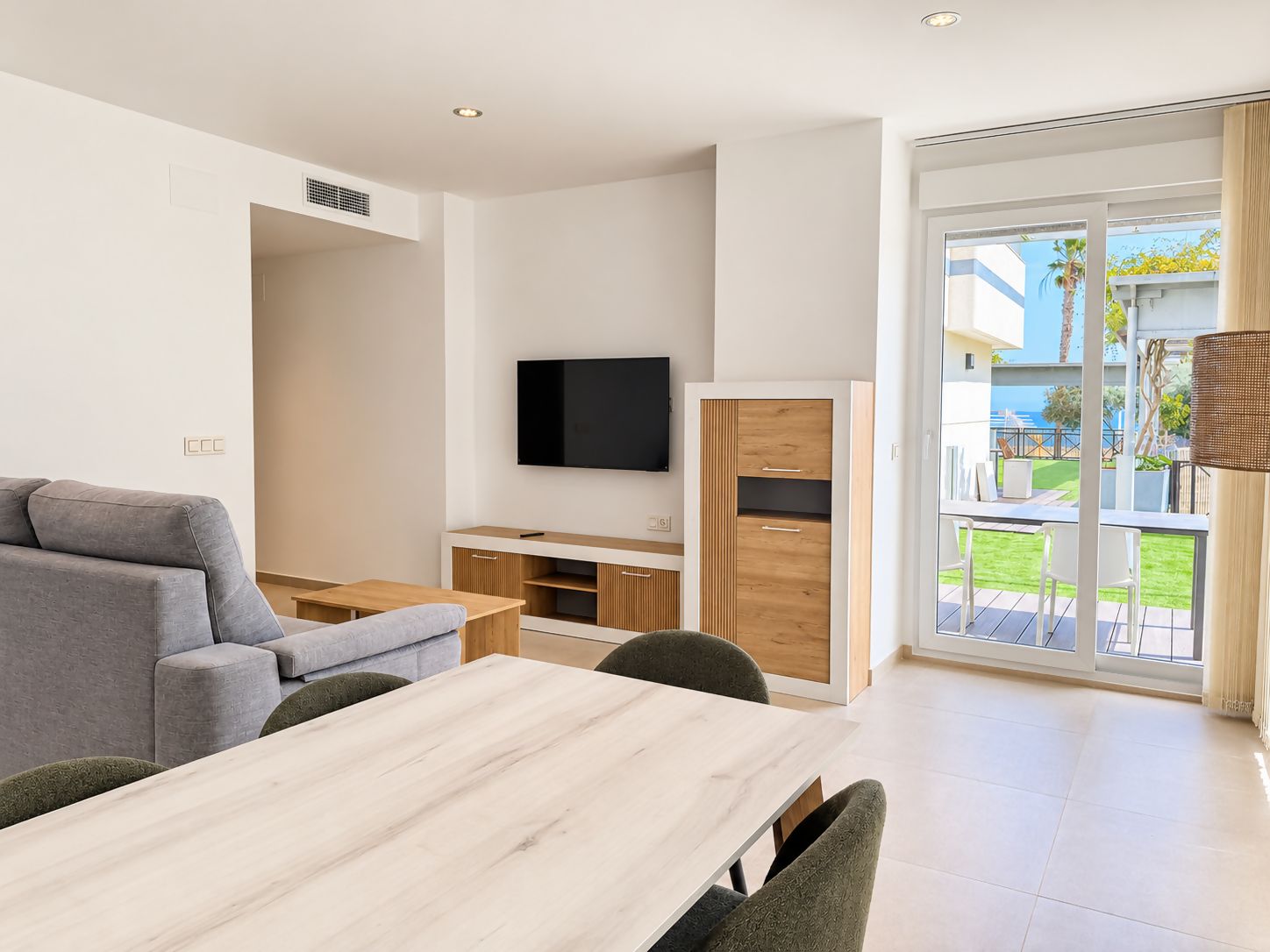 A modern living room with a sofa, a TV, a wooden cabinet, and a dining area with a table and chairs.
