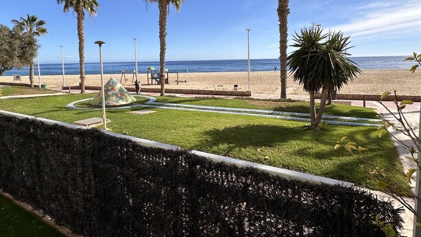 Blick auf einen Strand mit Palmen, einem Spielplatz und blauem Himmel.