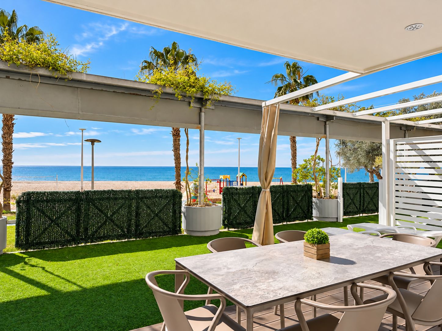 Une terrasse extérieure avec une table et des chaises, une vue sur la plage et une pergola blanche.