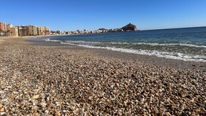 A pebbled beach with a clear blue sky and distant buildings. - Apartment 65B · Oceanfront with Private Terrace (Aguilas)