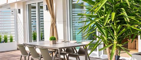 An outdoor patio with a dining table and chairs, a potted plant, and a view of the cityscape.