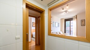 A hallway with white tiled walls, wooden flooring, and a mirror reflecting a bedroom with a bed and framed pictures. - M (SAM12) Fantastic one bedroom apartment in Madrid (Madrid)