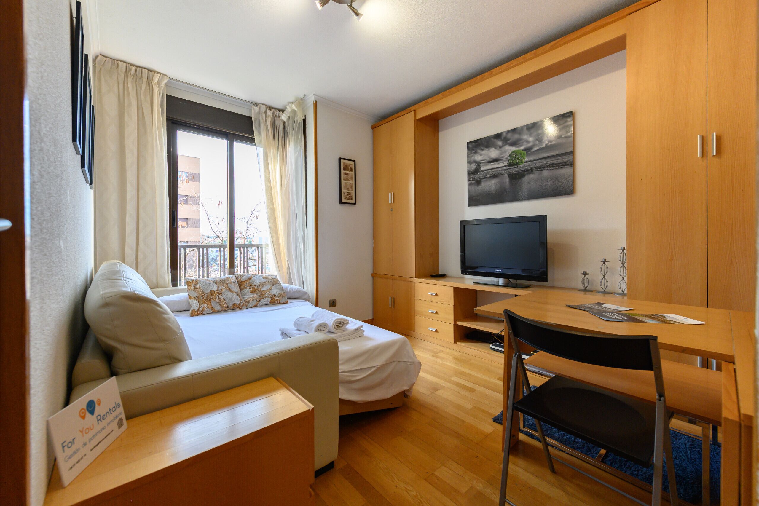 A hotel room with a bed, a desk, a television, and a window with curtains.