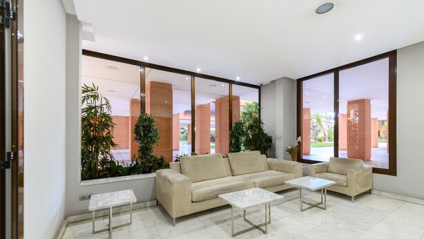 A spacious lobby with a beige sofa, two white coffee tables, and large windows offering a view of a brick building and greenery outside. - M (SAM12) Fantastic one bedroom apartment in Madrid (Madrid)