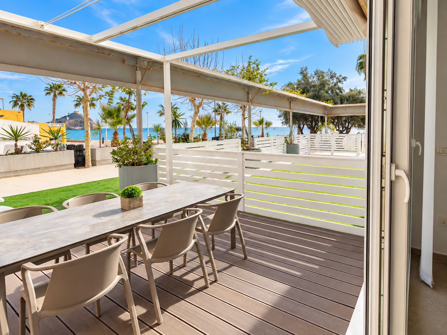 Un espace extérieur abrité, doté de sièges, offrant une vue sur la mer, avec une terrasse en bois et une balustrade blanche.