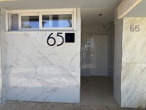 A building entrance with a marble facade, a number '65' sign, and a door leading inside. - Apartment 65A · Oceanfront with Private Terrace (Aguilas)