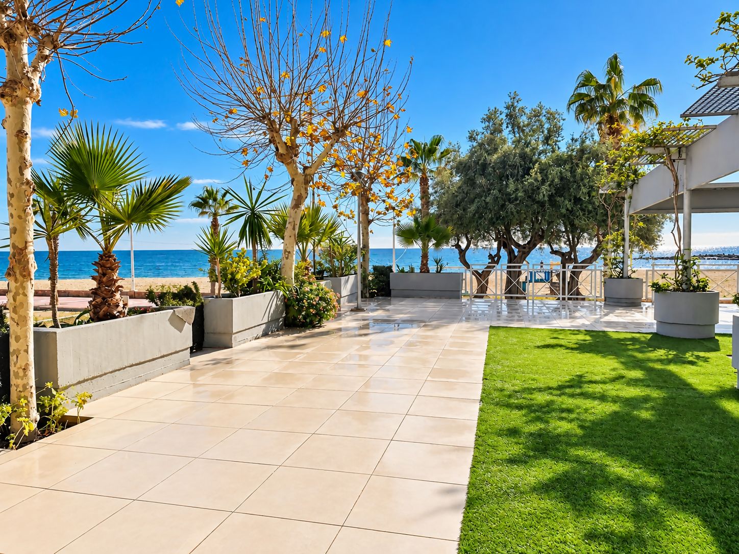 Une promenade dallée bordée d’une pelouse, de palmiers et offrant une vue sur la mer.
